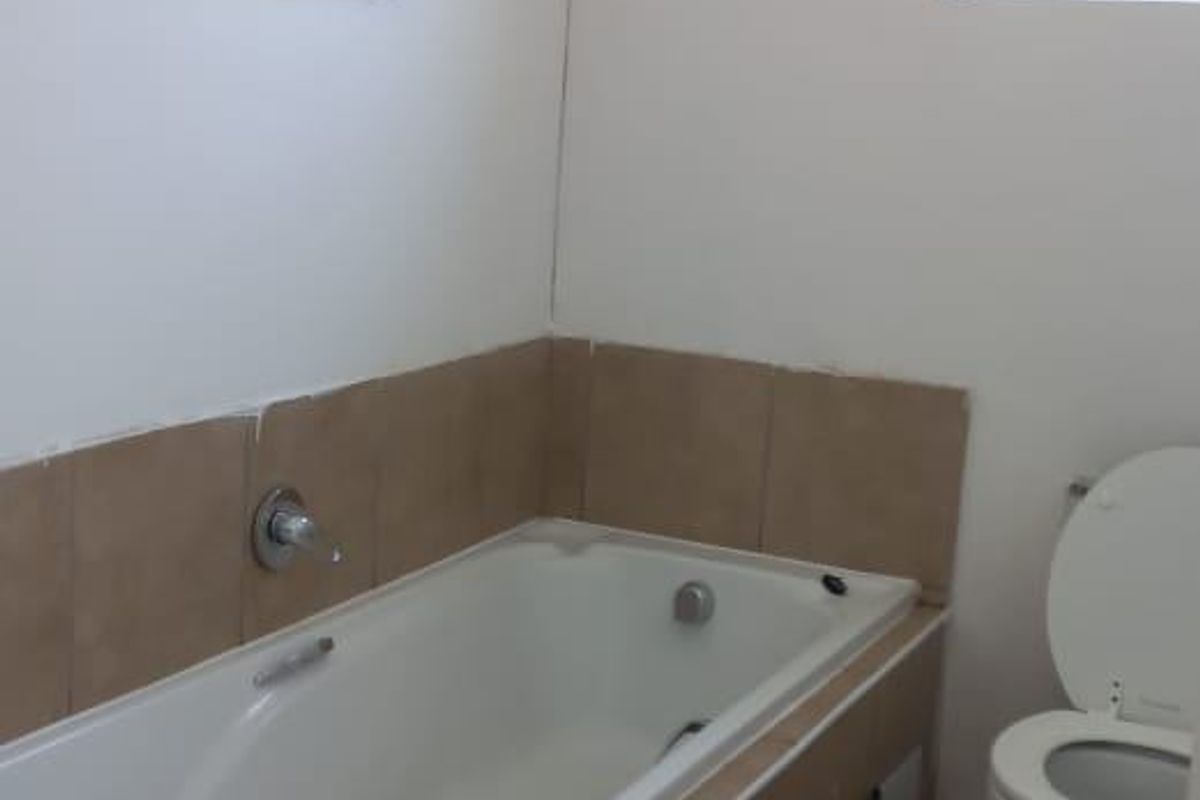 A functional bathroom featuring a built-in bathtub, toilet, and tiled finishes, offering a blank canvas for potential modernization and renovation.