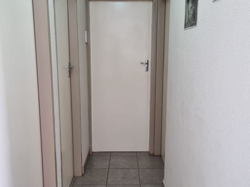 A clean and functional hallway featuring neutral tiled flooring and multiple internal doors providing access to various rooms.