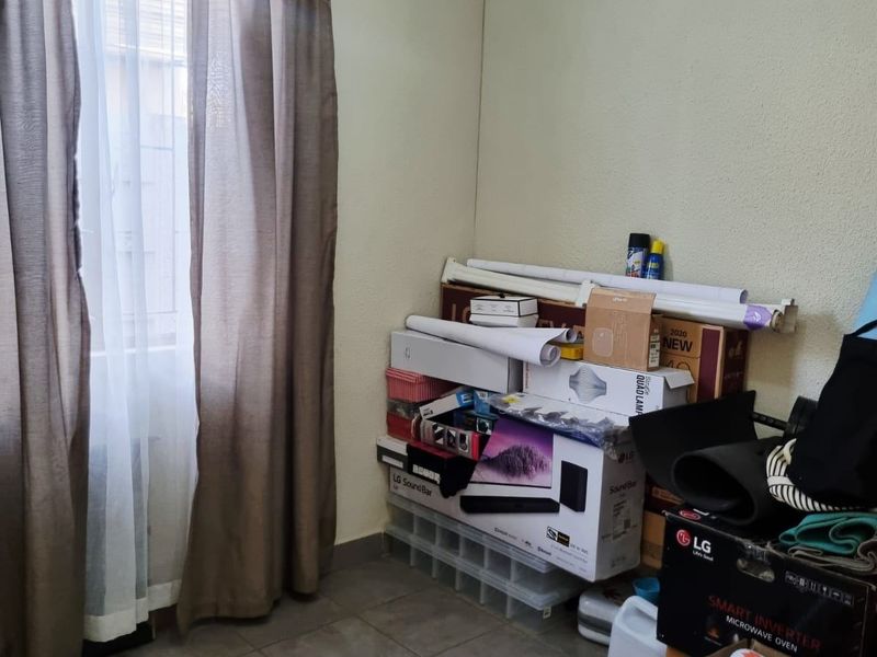 A bedroom featuring tiled flooring and a window with security bars, currently used for storage.