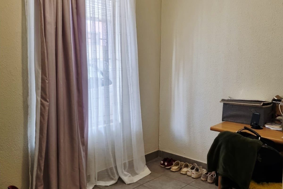 A functional bedroom space featuring neutral wall finishes, tiled flooring, and a window fitted with a curtain rod.