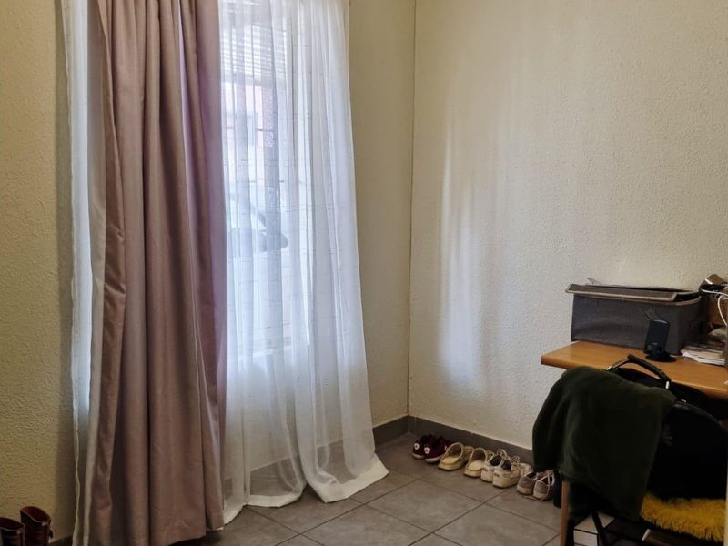 A functional bedroom space featuring neutral wall finishes, tiled flooring, and a window fitted with a curtain rod.