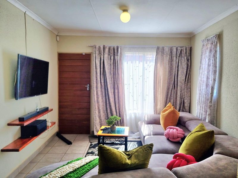 A cozy living room featuring tiled flooring, a timber entrance door, and wall-mounted shelving, providing a functional and comfortable living space.