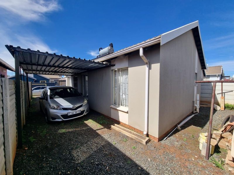 Side view of the property featuring a metal carport, solar geyser installation, and concrete boundary walling.
