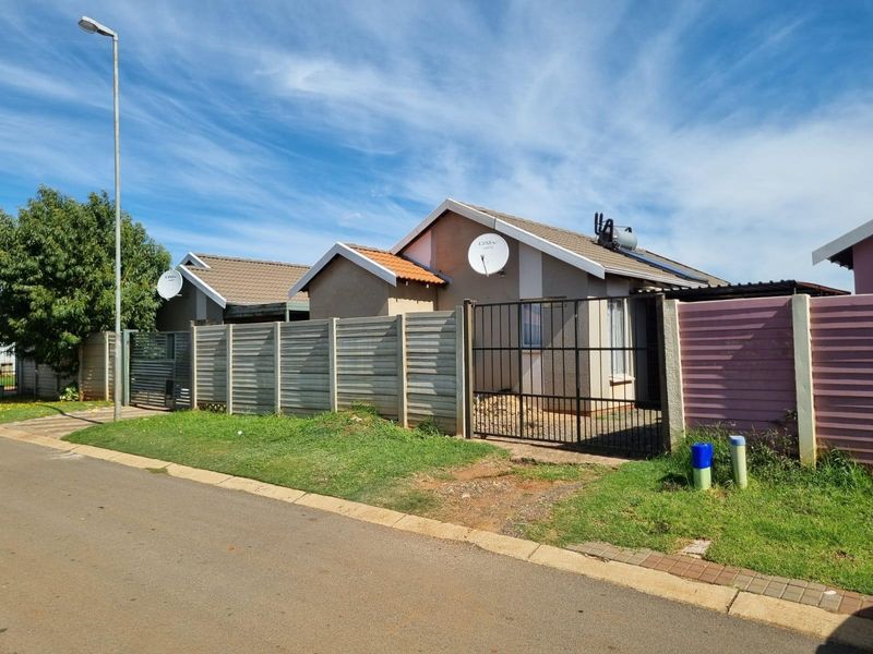 Front exterior view of a residential property featuring a tiled roof, solar water heater, and secure perimeter fencing with a metal driveway gate.