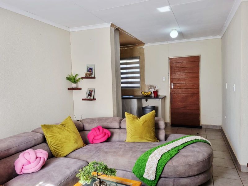 A living area featuring tiled floors and a wooden door, with an adjacent kitchenette area visible. The space requires minor finishing work on wall edges.