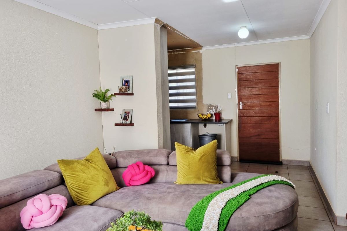 A living area featuring tiled floors and a wooden door, with an adjacent kitchenette area visible. The space requires minor finishing work on wall edges.