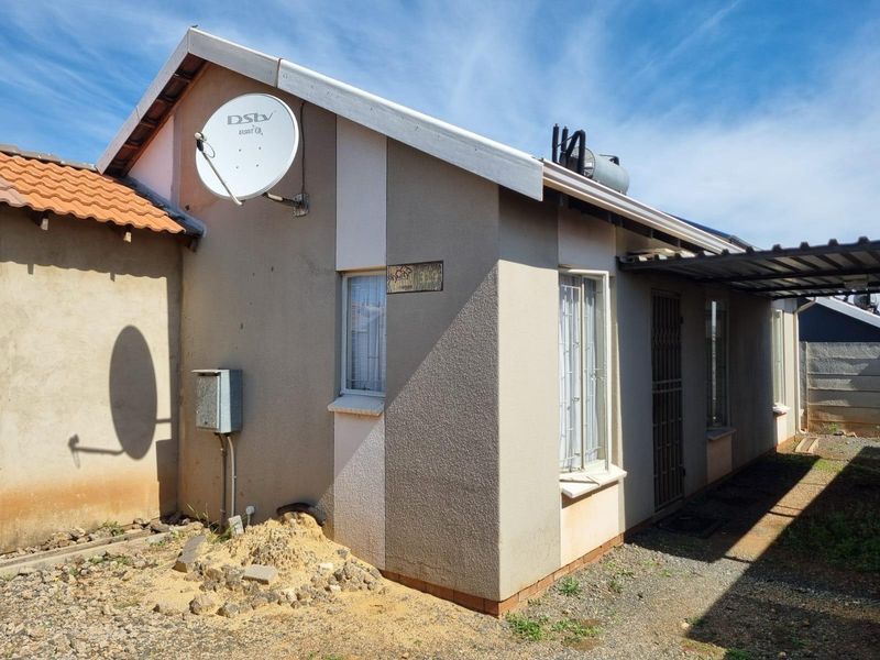Rear view of the property featuring plastered walls, a solar geyser, and a security gate, with an adjacent gravel area.