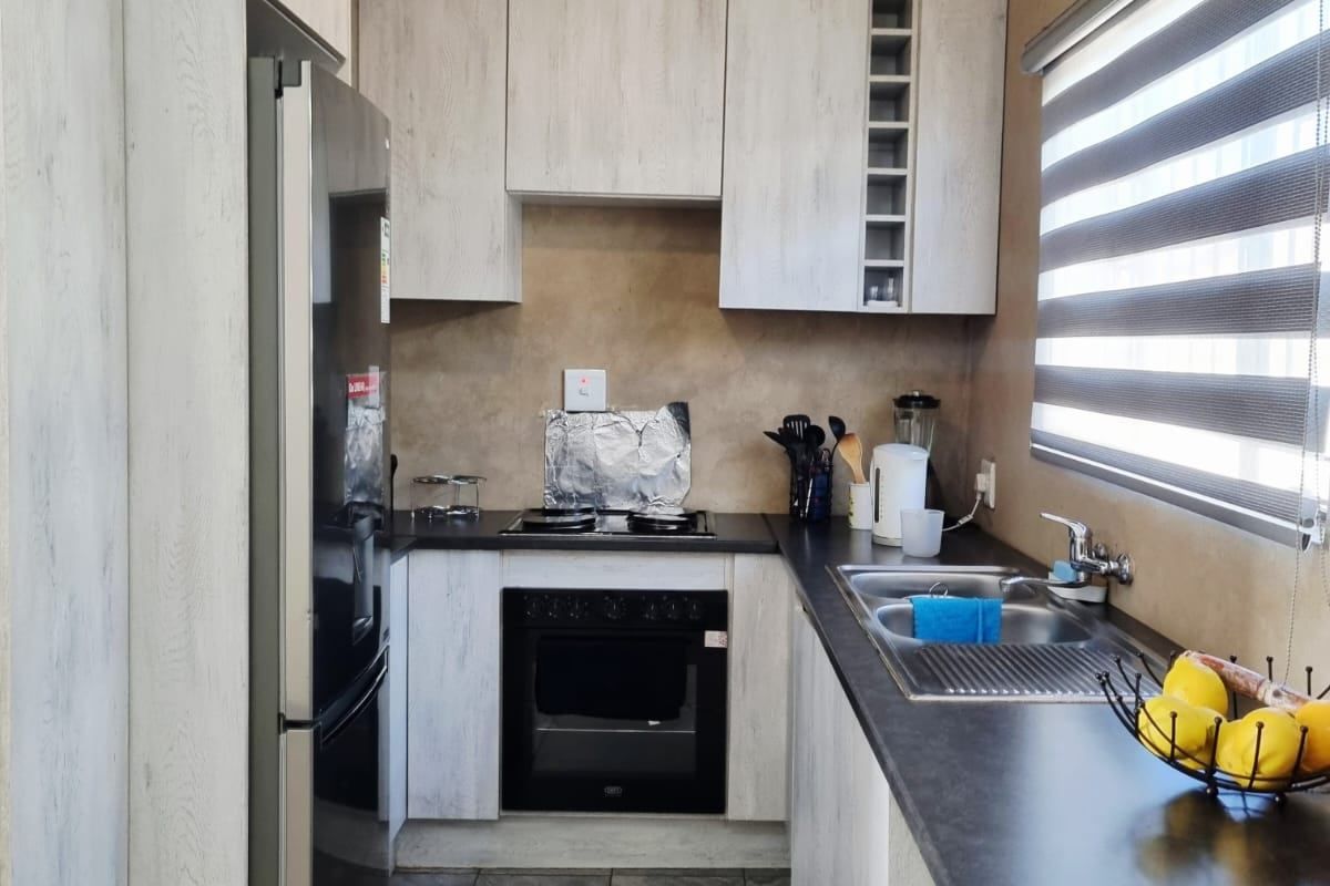 Compact kitchen featuring light wood-grain cabinetry, dark countertops, and built-in appliances, currently requiring ceiling and wall finishing to complete the space.
