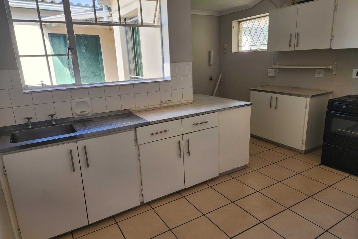 A functional kitchen featuring tiled flooring, laminate countertops, built-in cabinetry, and a stainless steel sink, offering a blank canvas for renovation.