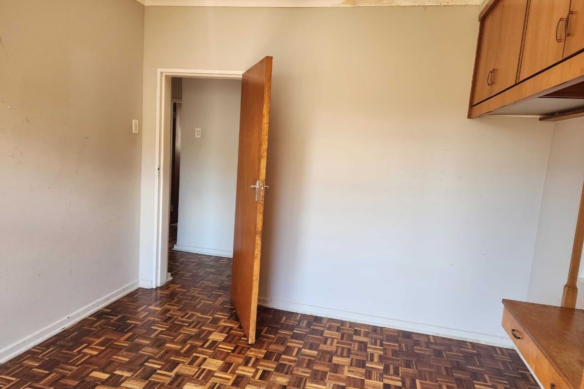 An empty bedroom featuring classic parquet flooring and built-in wooden cabinetry, requiring some cosmetic attention to the ceiling and walls.