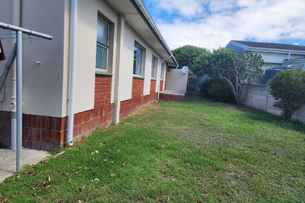 A view of the rear exterior of the house featuring a brick and plastered facade, a lawn area, and a concrete boundary wall.