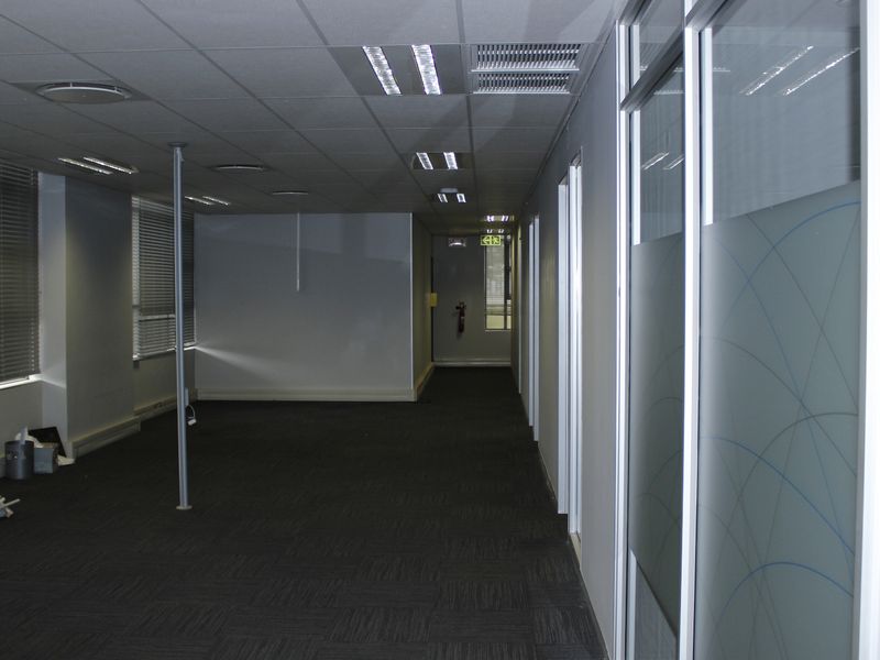 An empty commercial office space featuring carpet tiles, suspended ceilings with recessed lighting, and glass partition walls with privacy film.