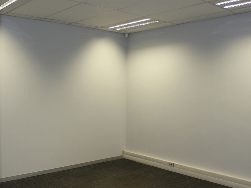 A clean, empty office space featuring neutral walls, carpeted flooring, and a suspended ceiling with integrated lighting.