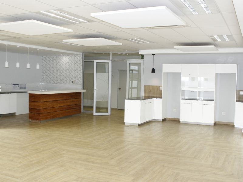 Spacious open-plan commercial area featuring modern laminate flooring, a suspended ceiling with recessed lighting, and integrated kitchen cabinetry with a sink.