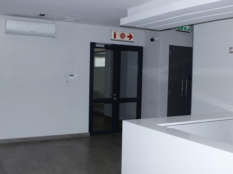 A clean and modern commercial entry area featuring tiled flooring, a built-in reception desk, and glass-panelled doors.