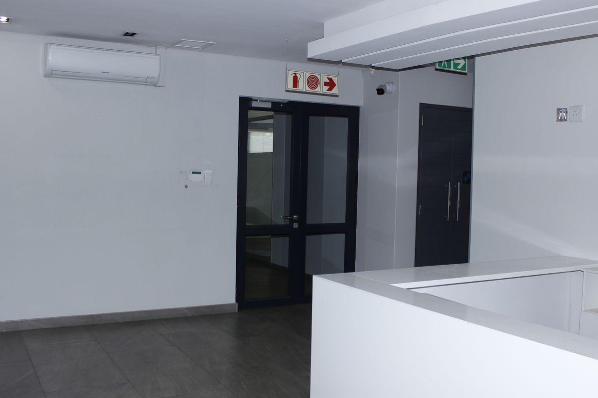 A clean and modern commercial entry area featuring tiled flooring, a built-in reception desk, and glass-panelled doors.