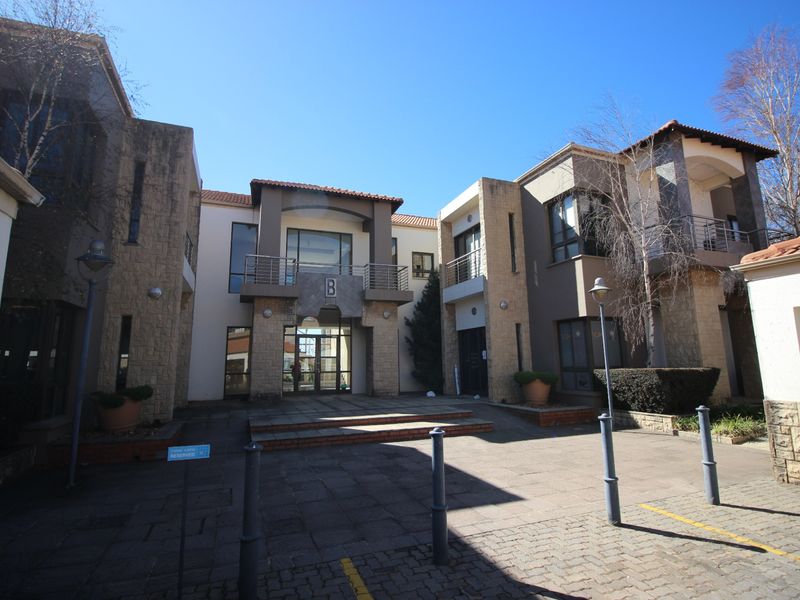 Front elevation of a commercial office building featuring stone cladding, paved courtyard entrance, and upper-level balconies.
