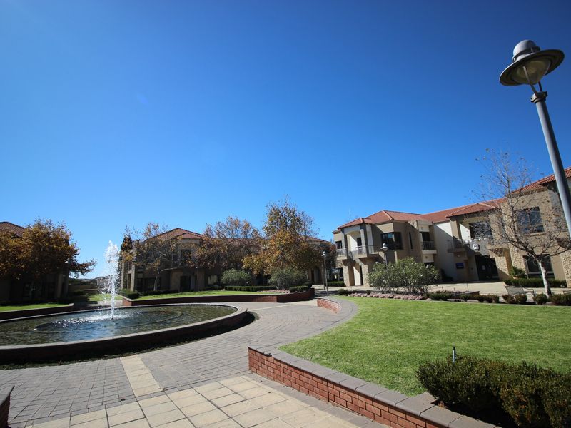 A well-maintained commercial office park courtyard featuring a central water fountain, paved walkways, manicured lawns, and brick retaining walls.