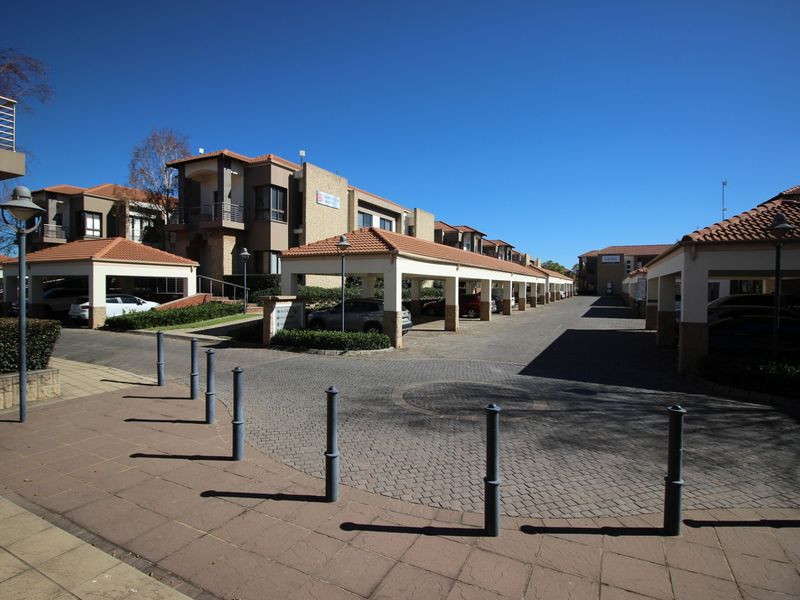 A well-maintained commercial complex featuring extensive covered parking bays, paved driveways, and professional exterior landscaping under a clear sky.