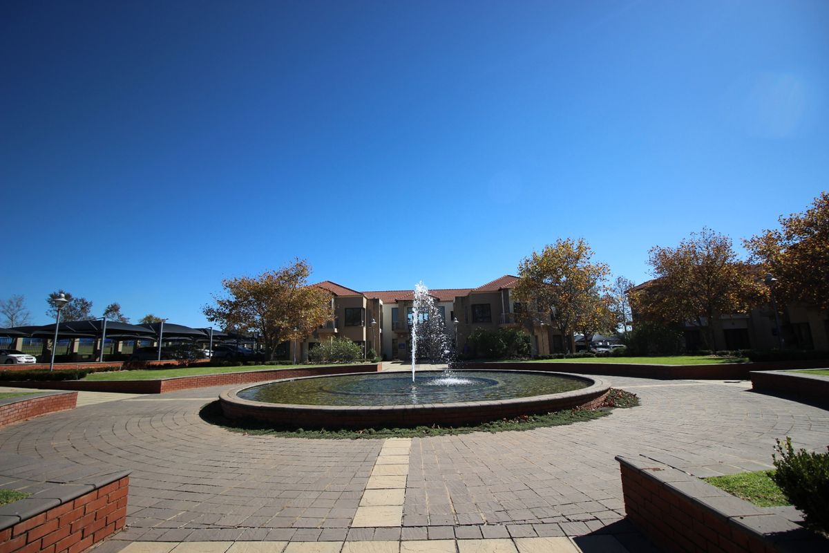 A well-maintained commercial office park entrance featuring a central circular water fountain, brick paved courtyard, and landscaped garden areas.