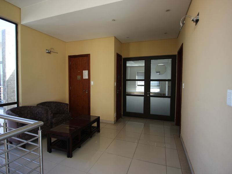 A bright commercial hallway featuring tiled flooring, recessed lighting, and glass-panelled double doors leading to an office space.