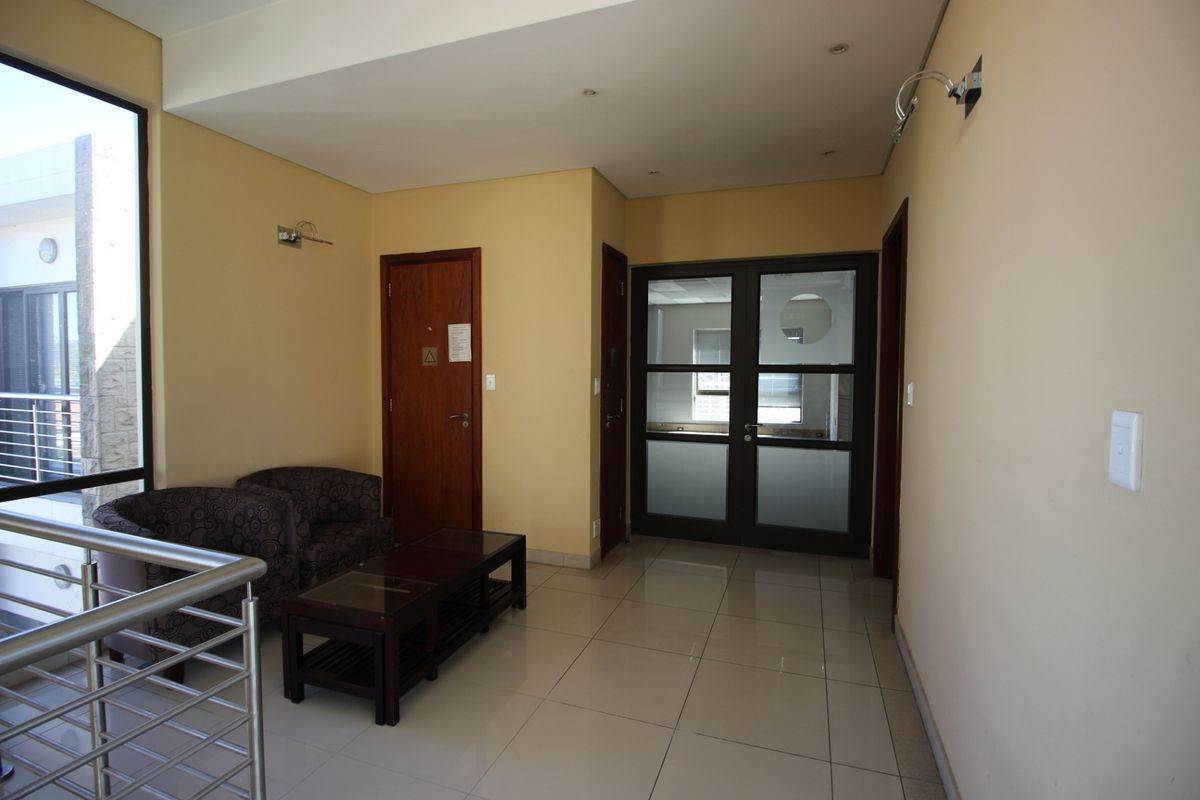 A bright commercial hallway featuring tiled flooring, recessed lighting, and glass-panelled double doors leading to an office space.