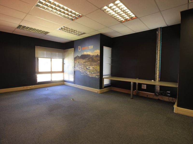 Empty commercial office space featuring a built-in desk, suspended ceiling with recessed lighting, and carpeted flooring, suitable for a professional workspace.
