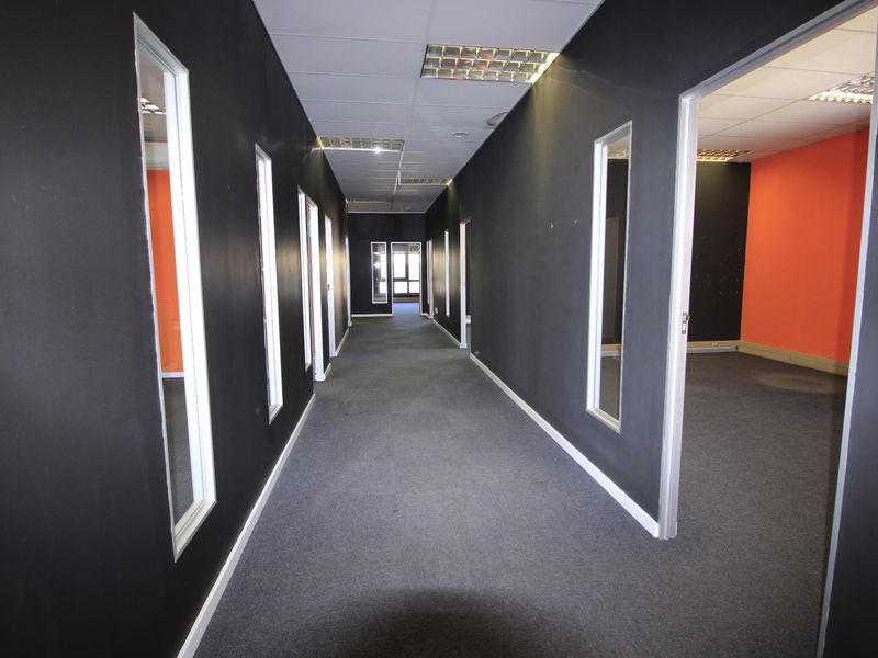 A commercial hallway featuring dark painted walls, carpeted flooring, and recessed ceiling lighting, providing access to multiple office spaces.