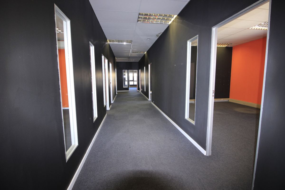 A commercial hallway featuring dark painted walls, carpeted flooring, and recessed ceiling lighting, providing access to multiple office spaces.