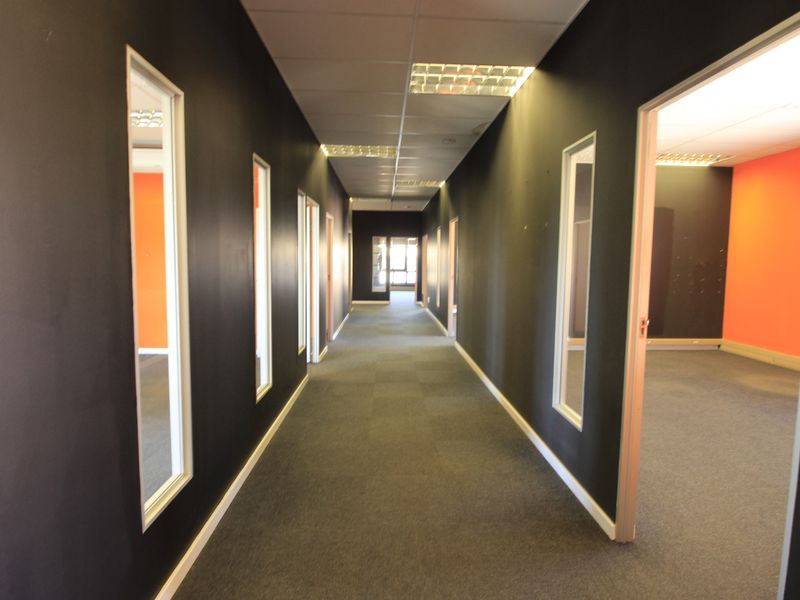 A long commercial office hallway featuring dark painted walls, carpeted flooring, and recessed lighting, providing access to multiple adjacent office spaces.