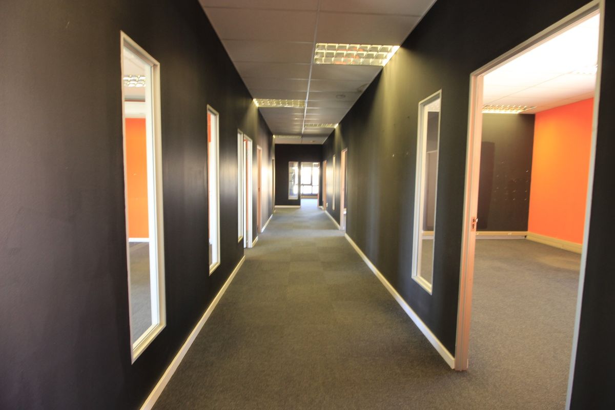A long commercial office hallway featuring dark painted walls, carpeted flooring, and recessed lighting, providing access to multiple adjacent office spaces.