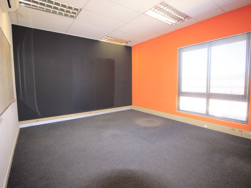 A vacant office space featuring carpeted flooring, a wall-mounted whiteboard, recessed ceiling lighting, and large windows with venetian blinds.