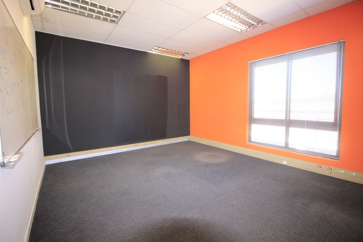 A vacant office space featuring carpeted flooring, a wall-mounted whiteboard, recessed ceiling lighting, and large windows with venetian blinds.