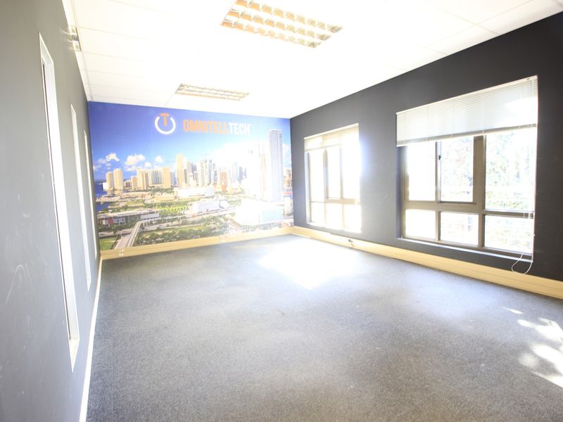 An empty commercial office space featuring large windows with blinds, recessed ceiling lighting, and carpeted flooring, suitable for a professional workspace.