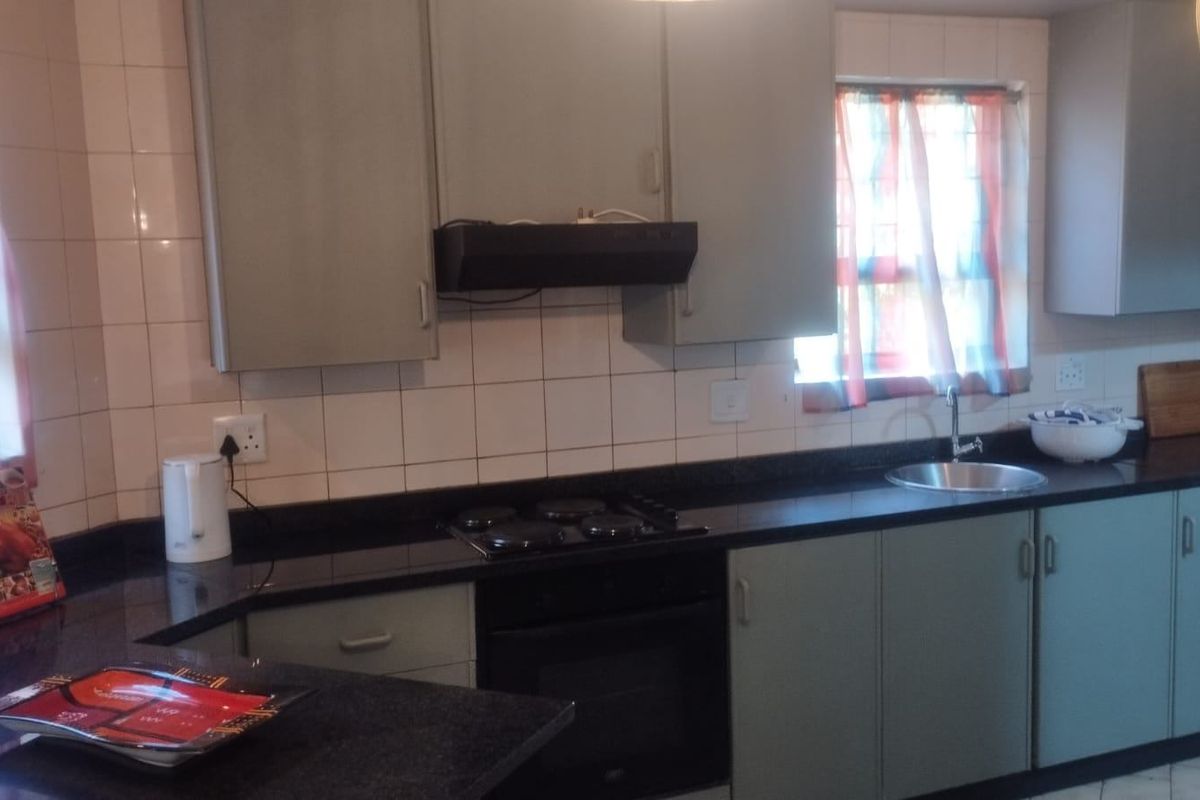 A functional kitchen featuring built-in cabinetry, granite countertops, an electric hob with extractor fan, and a stainless steel sink with tiled backsplash.