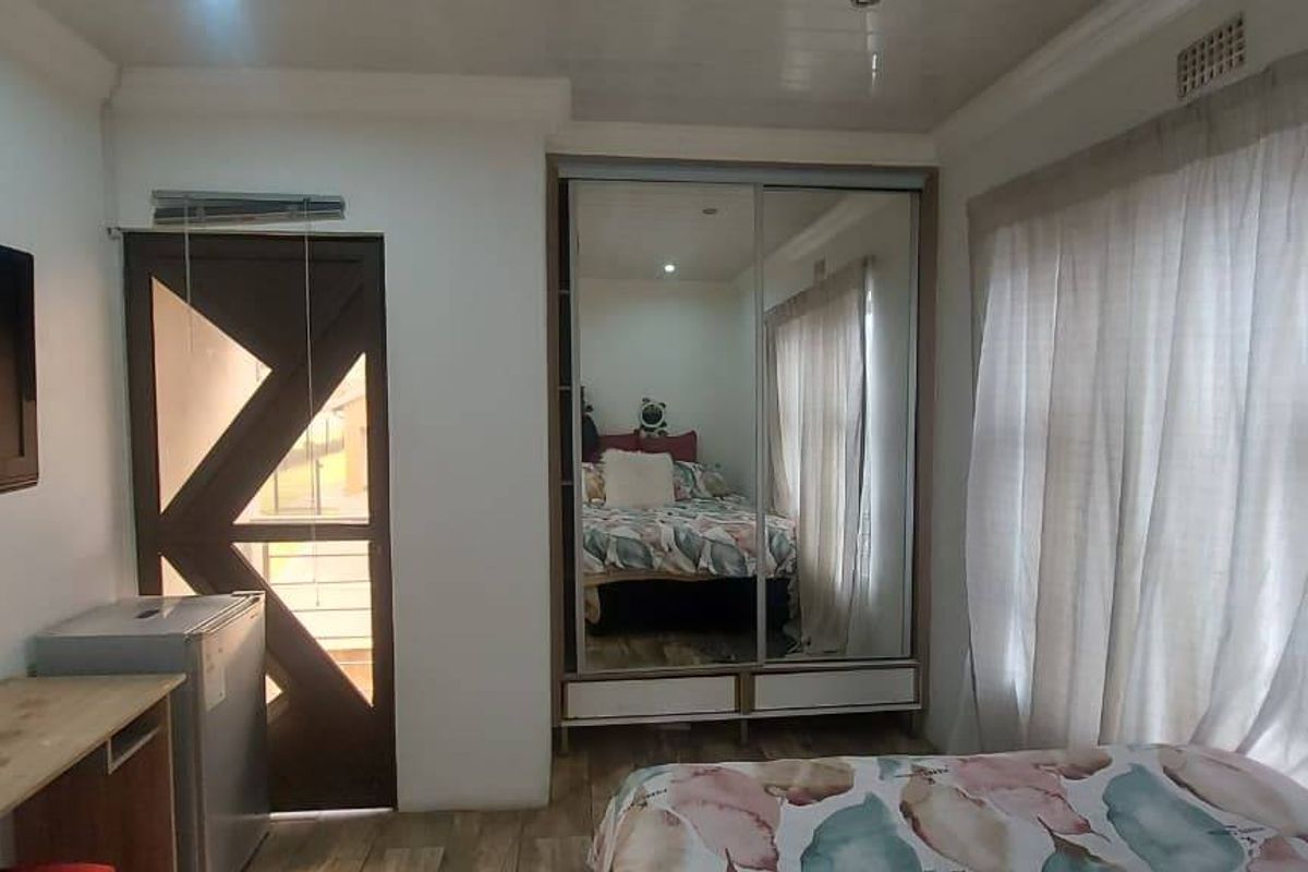 A bedroom featuring laminate flooring, built-in mirrored wardrobes, and a ceiling panel finish, providing a functional and compact living space.