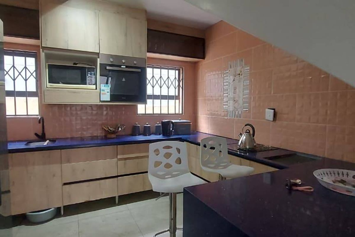 A functional kitchen featuring light wood-look cabinetry, dark countertops, a tiled backsplash, and built-in appliances, situated under a sloped ceiling.