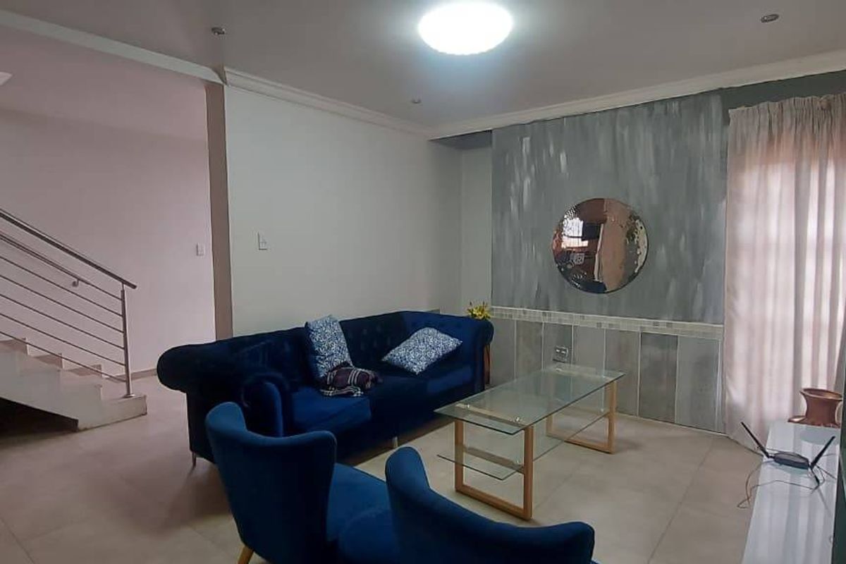 A living room featuring tiled flooring, a staircase with a stainless steel balustrade, and a decorative feature wall.