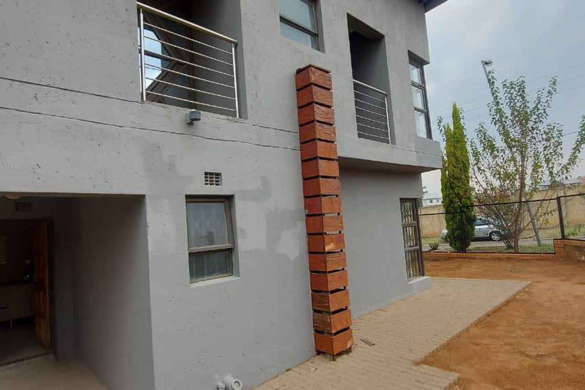 Rear view of a two-story house featuring a paved patio, stainless steel balcony railings, and a decorative brick column detail.