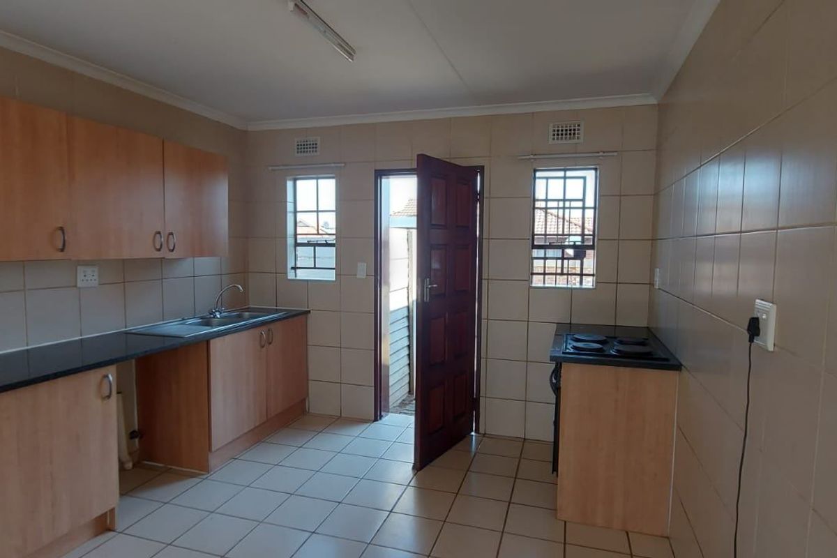 A functional, empty kitchen featuring built-in cabinetry, laminate countertops, and tiled finishes, offering a blank canvas for potential modern updates.