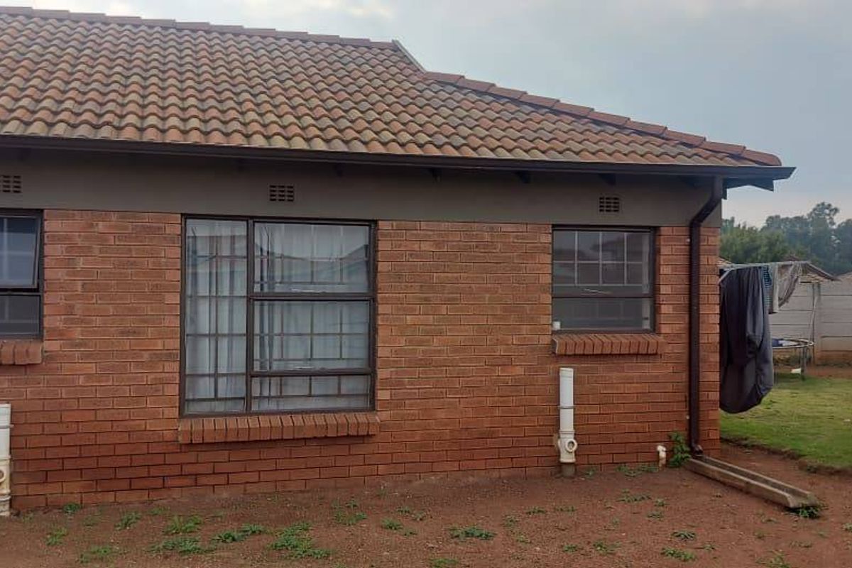 Rear view of a brick house featuring a tiled roof, aluminium windows, and a private garden area enclosed by a precast concrete boundary wall.