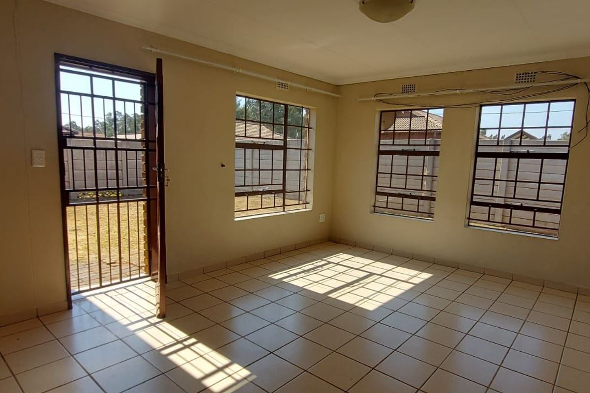An empty living room featuring tiled flooring, security gates, and burglar bars on the windows, offering a blank canvas for potential updates.