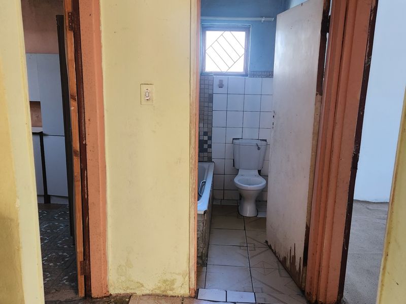 A view from a hallway looking into a bathroom, featuring tiled flooring and basic bathroom fixtures in need of cosmetic refurbishment.