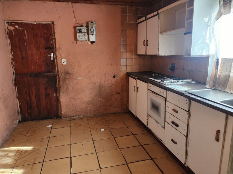 A dated kitchen featuring built-in cabinetry, an electric hob, and oven, requiring significant renovation and cosmetic updates to restore functionality and aesthetic appeal.