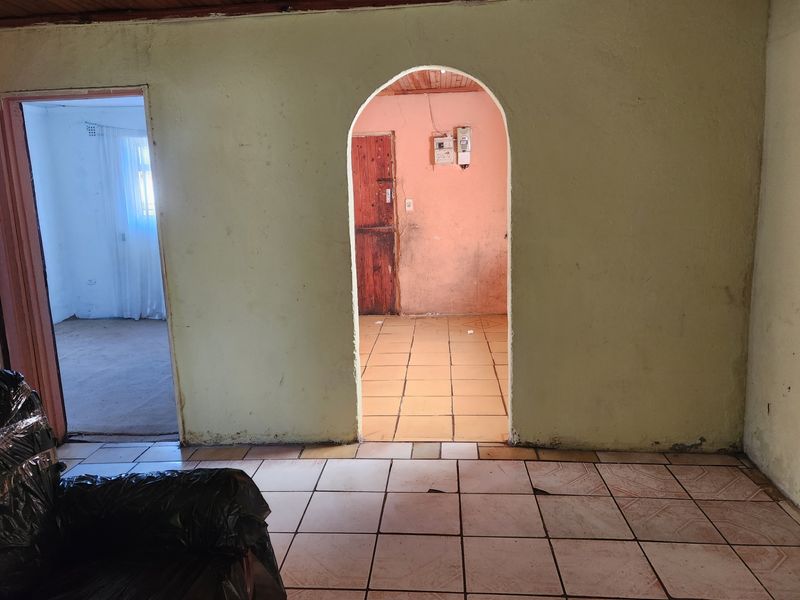 An interior living space featuring an arched doorway, ceramic tiled flooring, and a timber ceiling, currently in need of cosmetic renovation and repair.