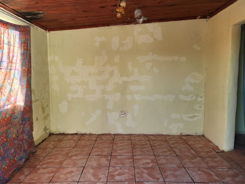An empty living room featuring ceramic floor tiles and a timber ceiling, currently requiring significant wall and ceiling repairs and cosmetic updates.