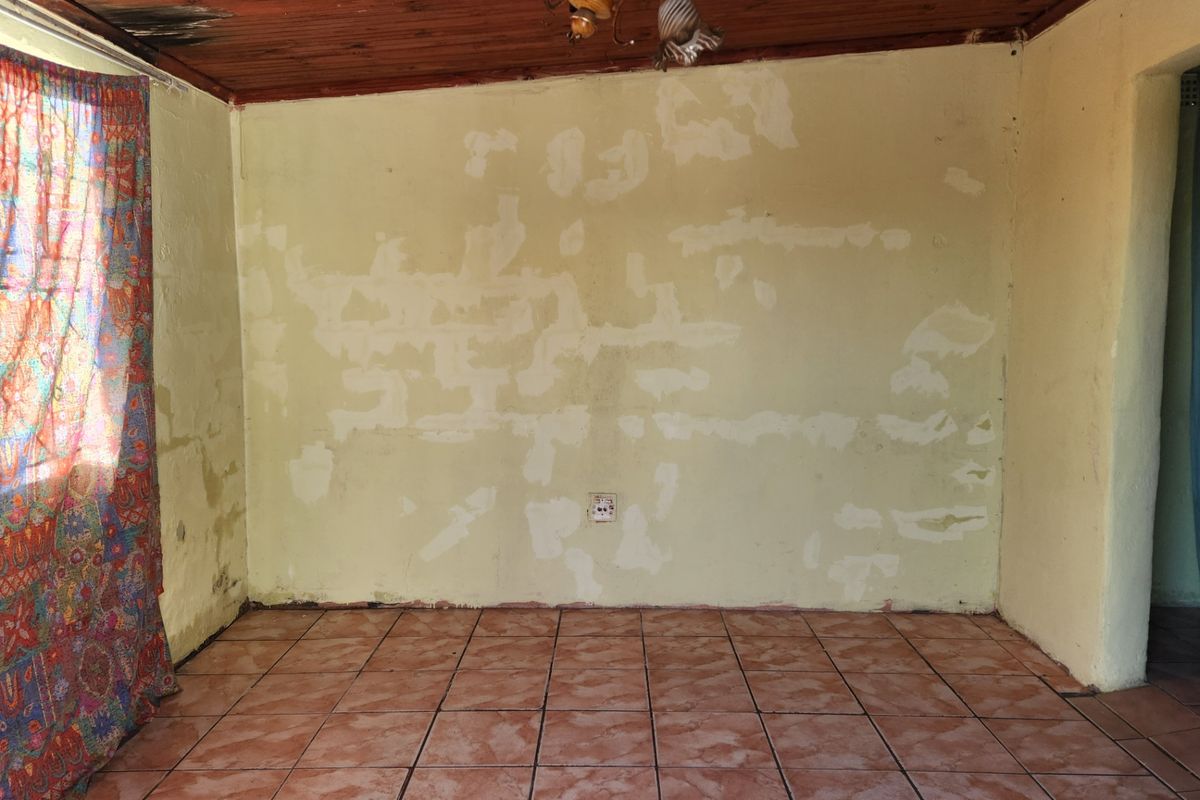 An empty living room featuring ceramic floor tiles and a timber ceiling, currently requiring significant wall and ceiling repairs and cosmetic updates.