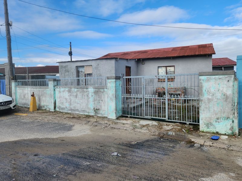 Front exterior view of a single-story house featuring a metal perimeter fence, gated entrance, and a corrugated metal roof.