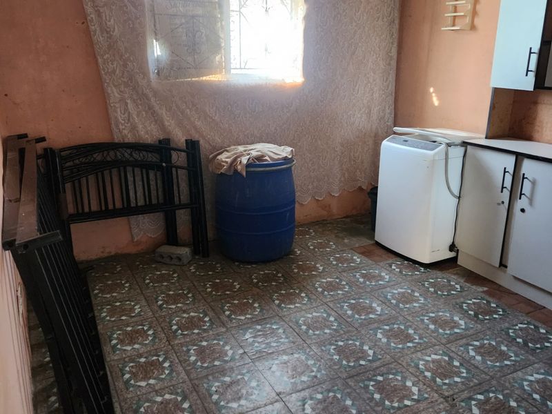 A functional laundry area featuring tiled flooring, built-in cabinetry, and a window with security bars, requiring cosmetic updates to improve its overall condition.