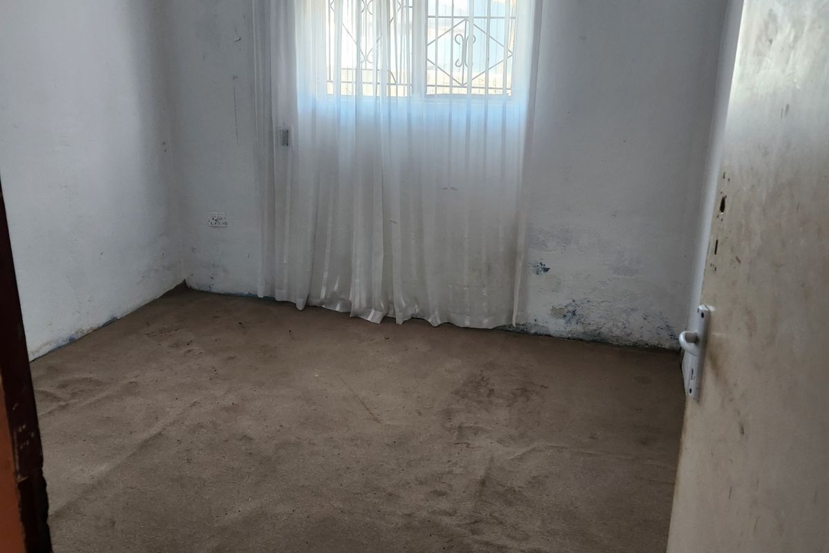 An empty bedroom featuring carpet flooring and a window with a security gate, requiring cosmetic updates and wall repairs.